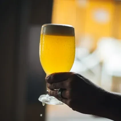 Close-up of hand holding a frothy golden beer glass, dripping liquid.