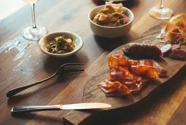 Charcuterie board with cured meats, olives, salad, and wine glasses.