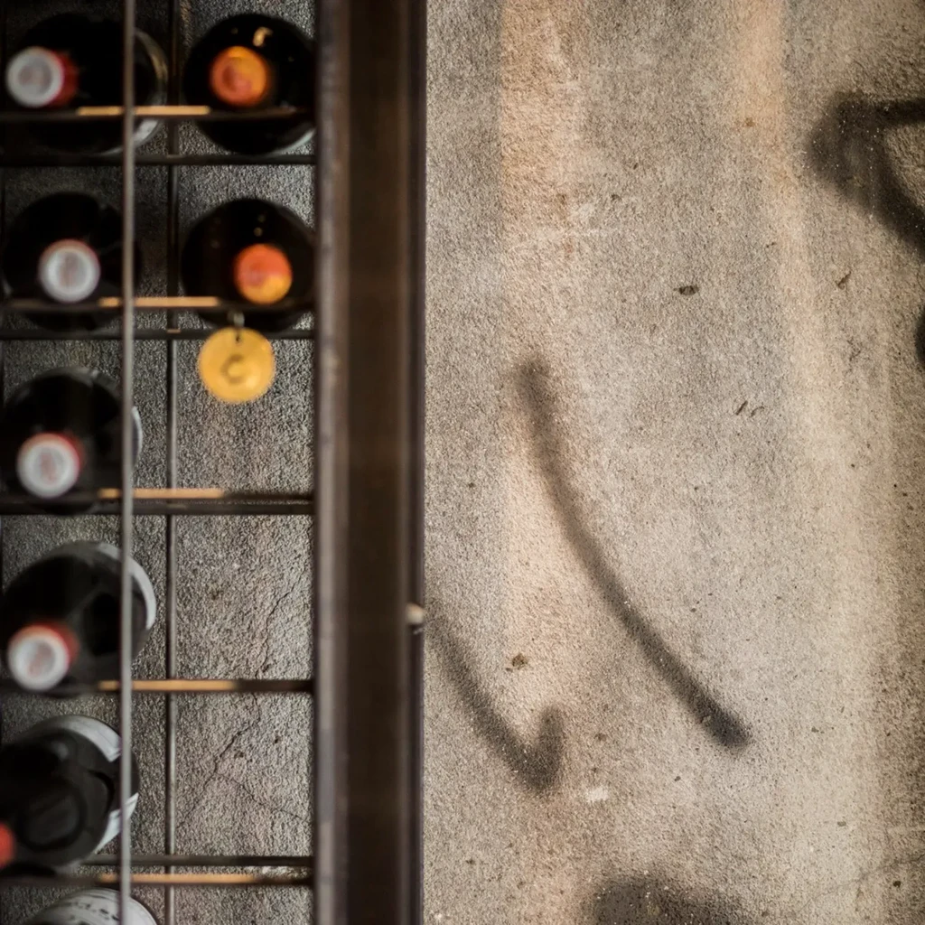 Dark metal wine rack with bottles beside a textured grey wall.