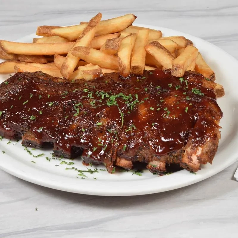 A plate of barbecue ribs covered in sauce with a side of fries.