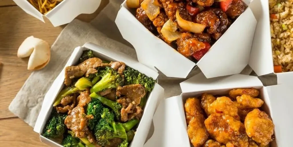 Multiple white takeout boxes filled with Chinese food and a fortune cookie.