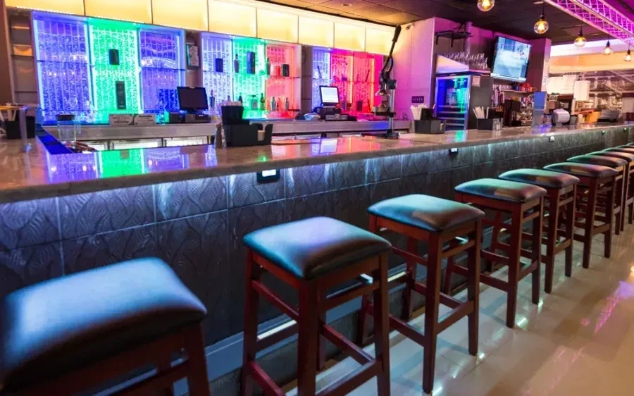 Long bar with stools, colorful light displays, and multiple screens.