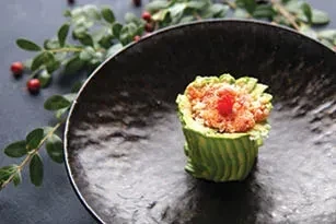 A small sushi roll wrapped in green, on a black plate.