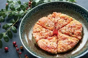 Cooked salmon fish cake sliced in a bowl, with berries and leaves.