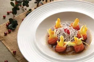 A white plate holds artfully arranged salmon and yellow peppers in sauce.