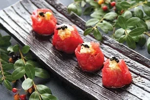 Four red tuna rolls with rice and black caviar on a wooden plate.