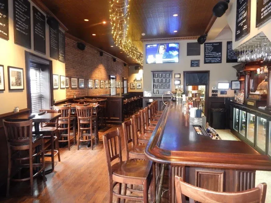 Interior of a long, narrow pub with exposed brick and string lights.