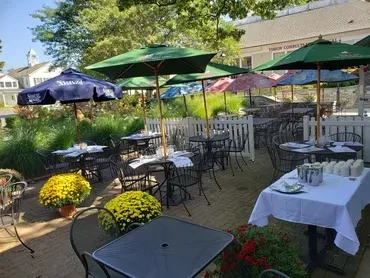 An outdoor patio with tables, chairs, and several green and colorful umbrellas.