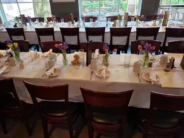 Long tables with white cloths and chairs in a restaurant dining room.