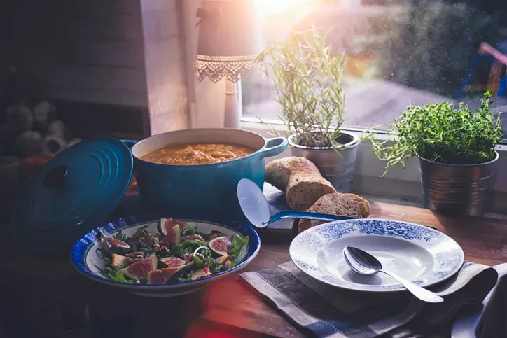Rustic food spread: orange soup in teal pot, salad, bread.