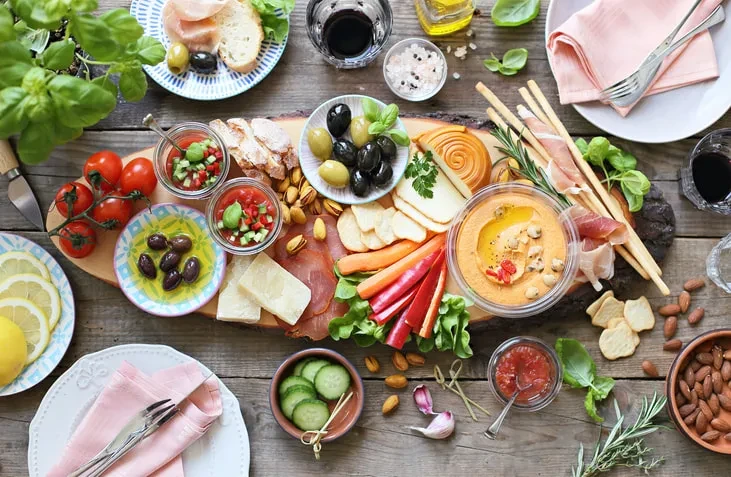 Overhead: Rustic table with charcuterie, cheeses, dips, and red wine.