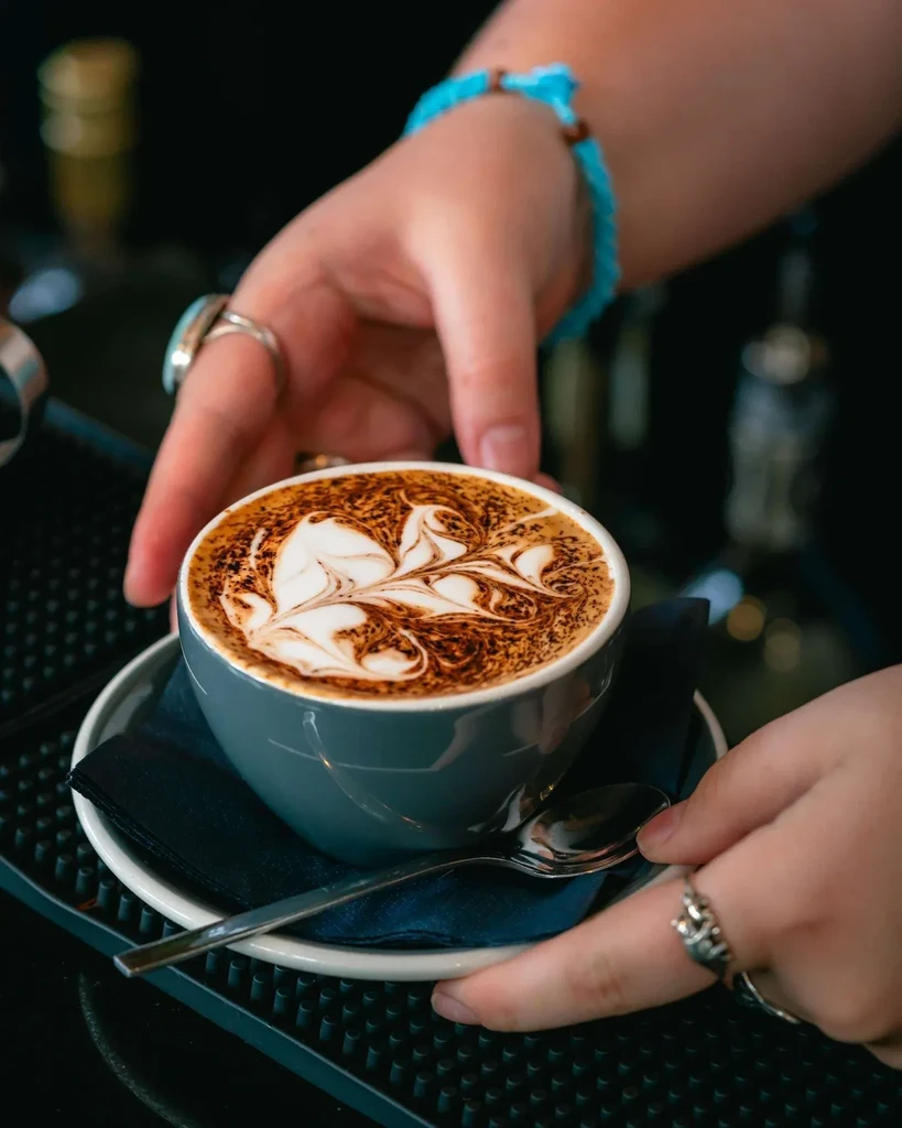 A barista's hands serve a latte with intricate foam art.