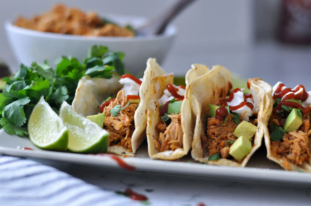 A plate of shredded chicken tacos with lime, avocado, and cilantro.