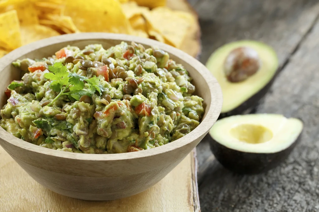 A wooden bowl of guacamole with avocado halves and tortilla chips.