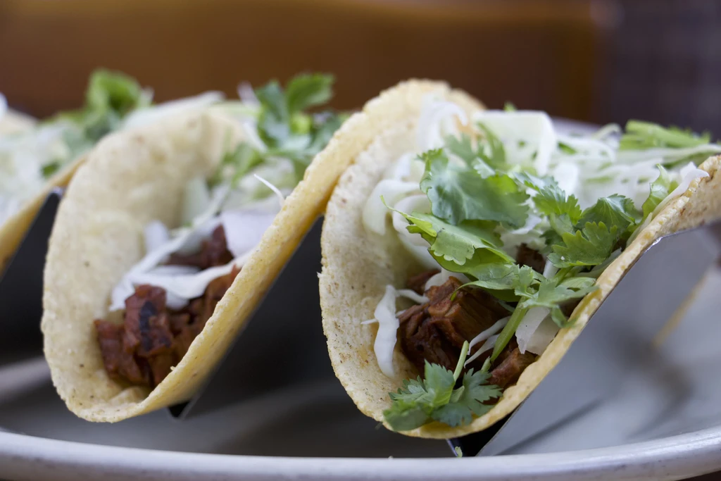 Two street tacos with meat, cabbage, and cilantro in holders.