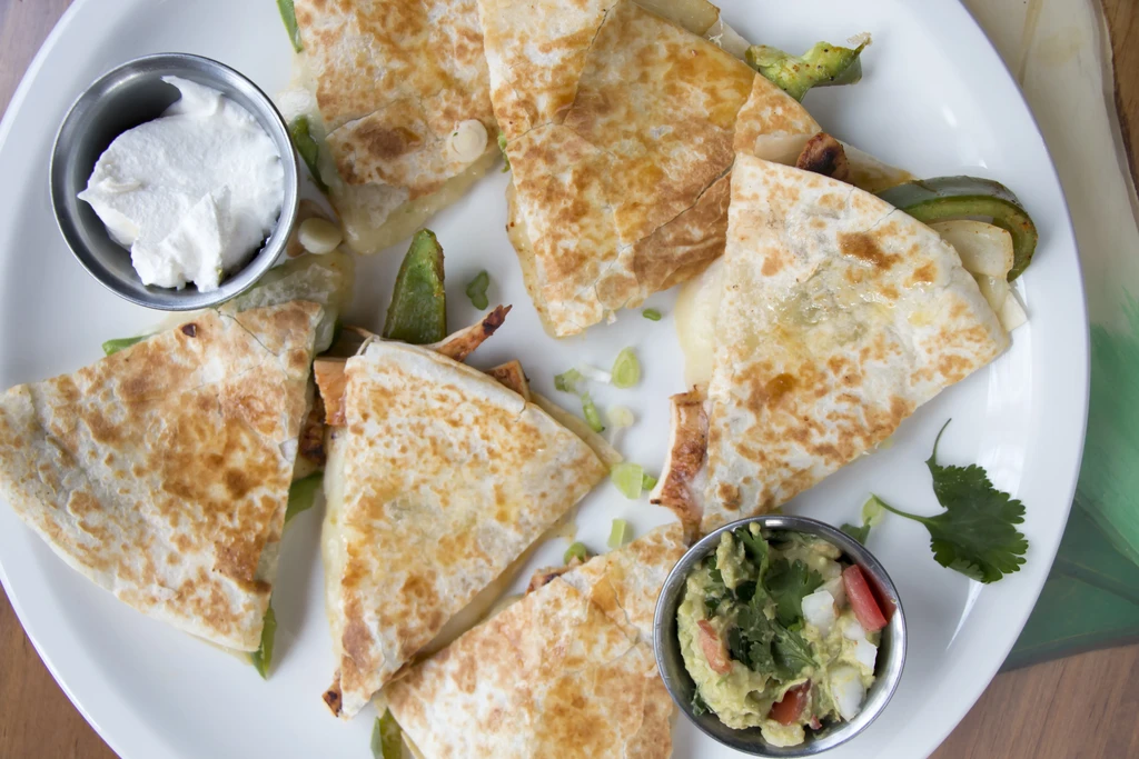 A plate of cheese quesadillas with sour cream and guacamole.