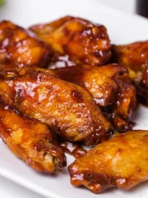 Several shiny, sauced chicken wings are arranged on a white plate.