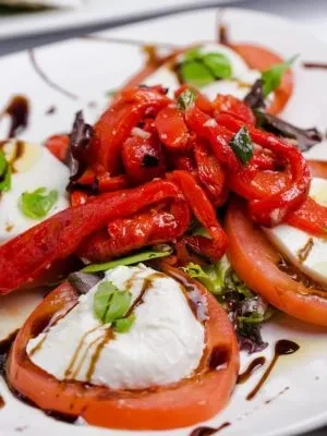 Caprese salad with sliced tomatoes, mozzarella, red peppers, and basil.