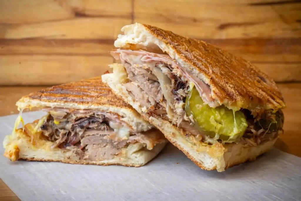A Cuban sandwich cut in half, revealing pork, ham, cheese, and pickles.