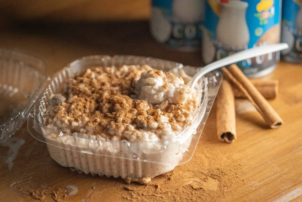Rice pudding with cinnamon in a plastic container, with cinnamon sticks.