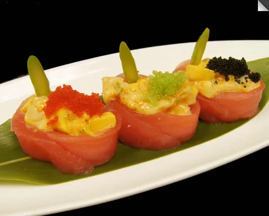 Three tuna sushi rolls with colorful toppings on a white plate.
