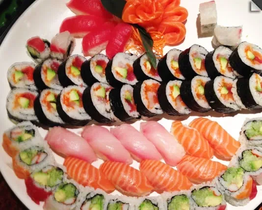 A white platter overflows with various colorful sushi and sashimi.
