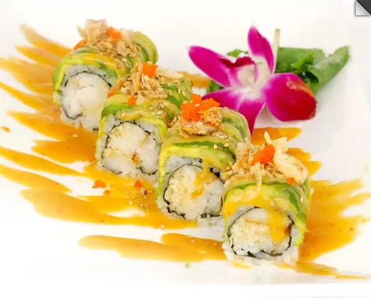 Sushi rolls topped with avocado and crunchy garnish, orange sauce, and orchid.