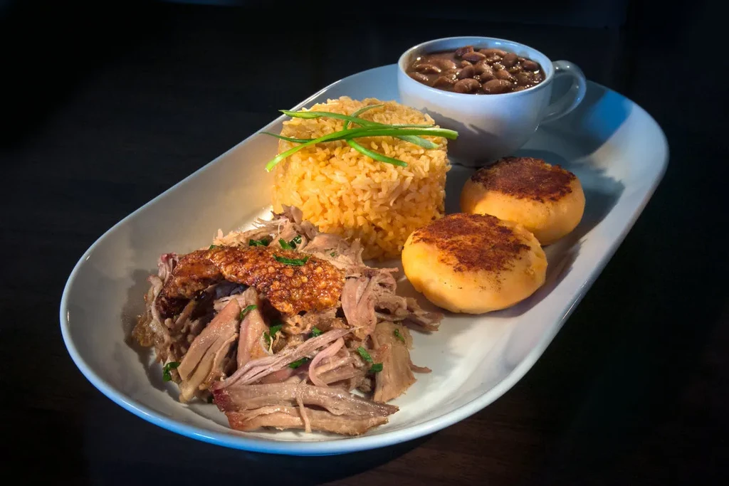 A plate of shredded pork with rice, beans, and two round cakes.
