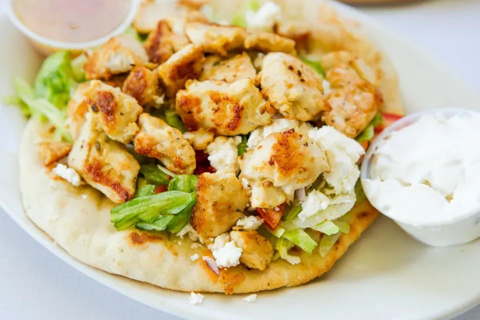 Pita bread topped with chicken, lettuce, feta, and two sauces.