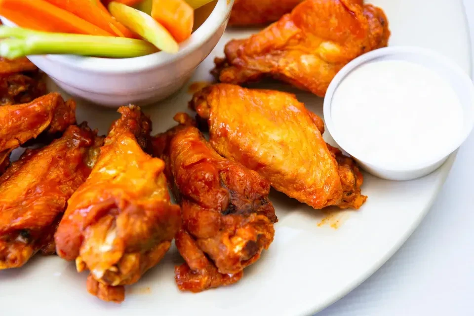 Buffalo wings on a white plate with celery, carrots, and dip.