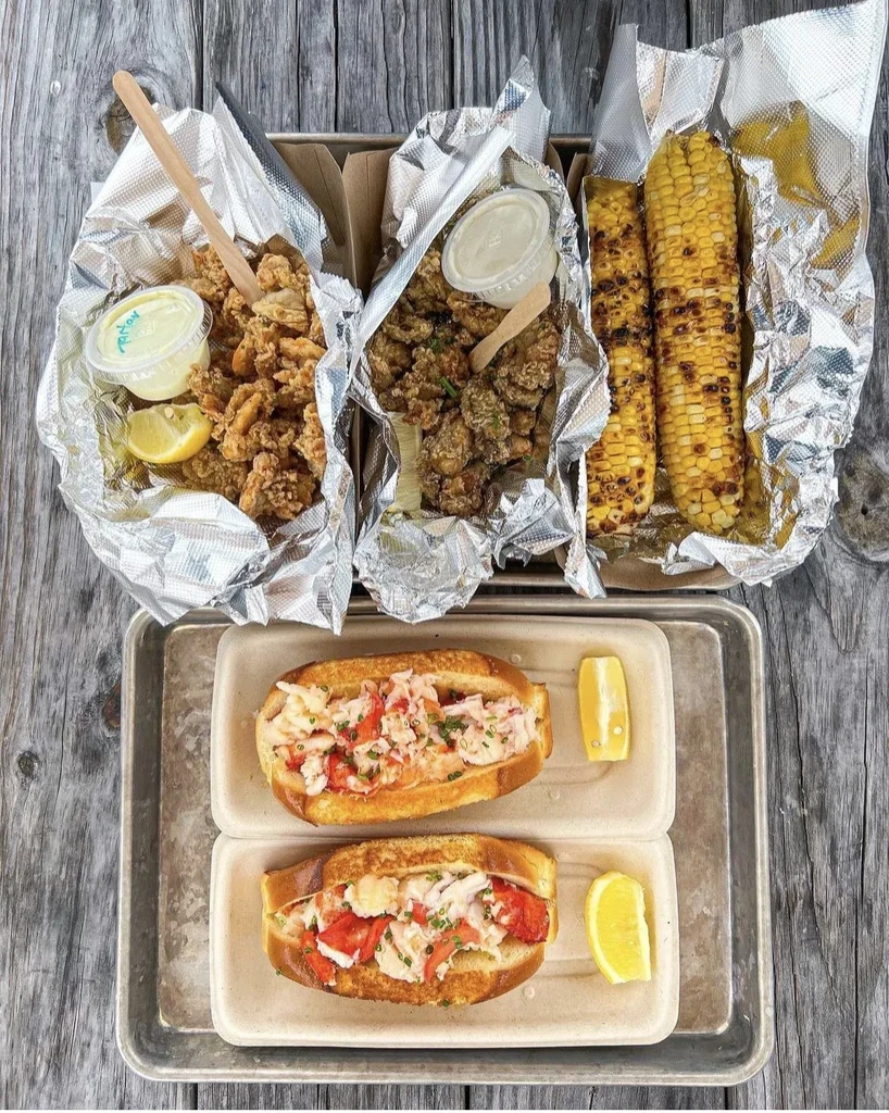 Seafood dinner with fried clams, corn, and lobster rolls on wooden table.