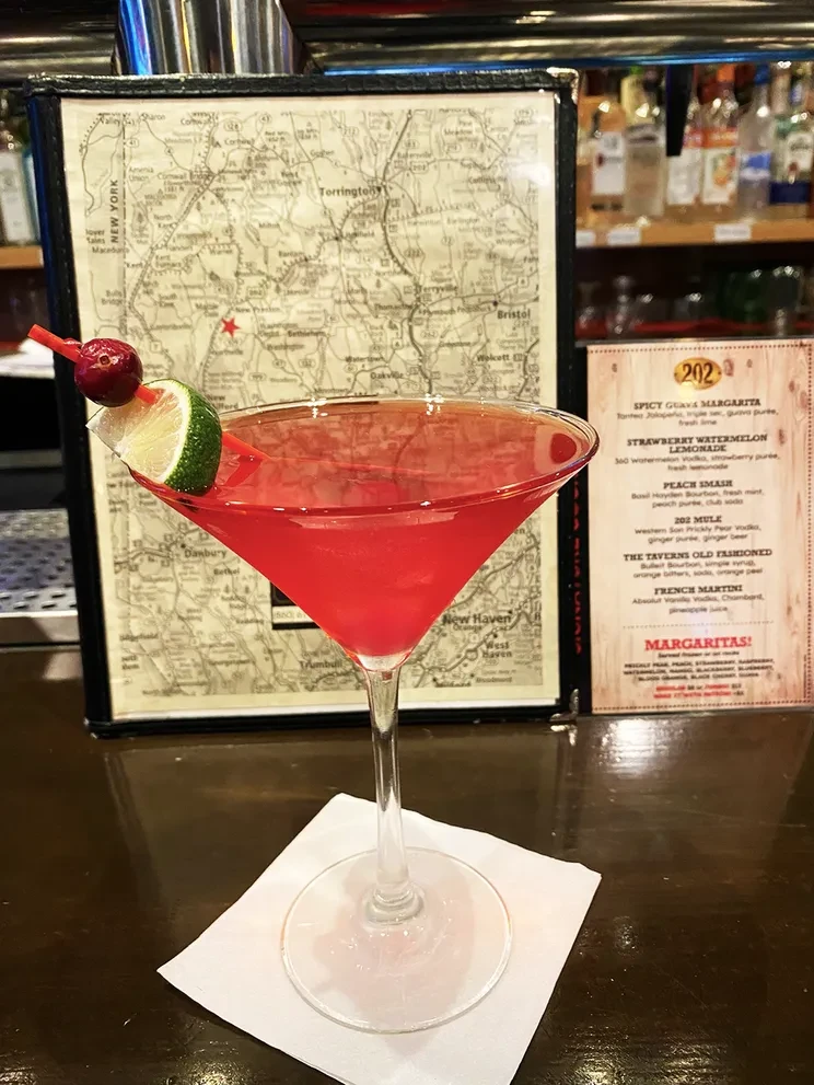 Red cocktail in martini glass with cherries on dark bar.