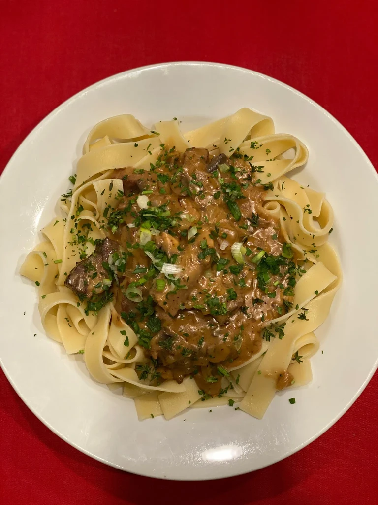 Pasta with creamy meat and mushroom sauce, garnished with fresh herbs.