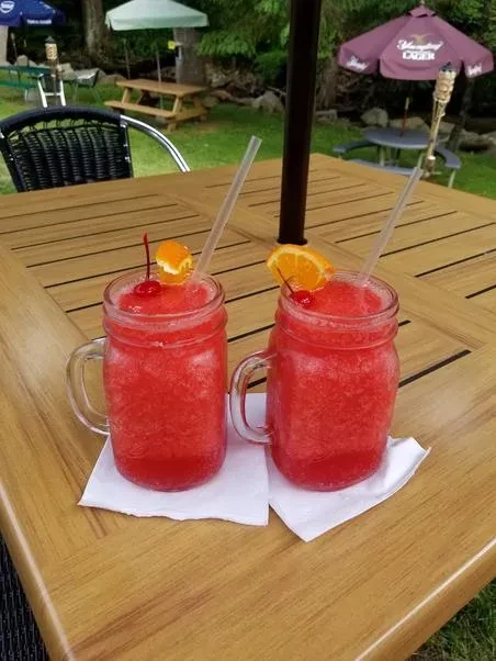 Two garnished frosty red drinks in mason jars on an outdoor table.