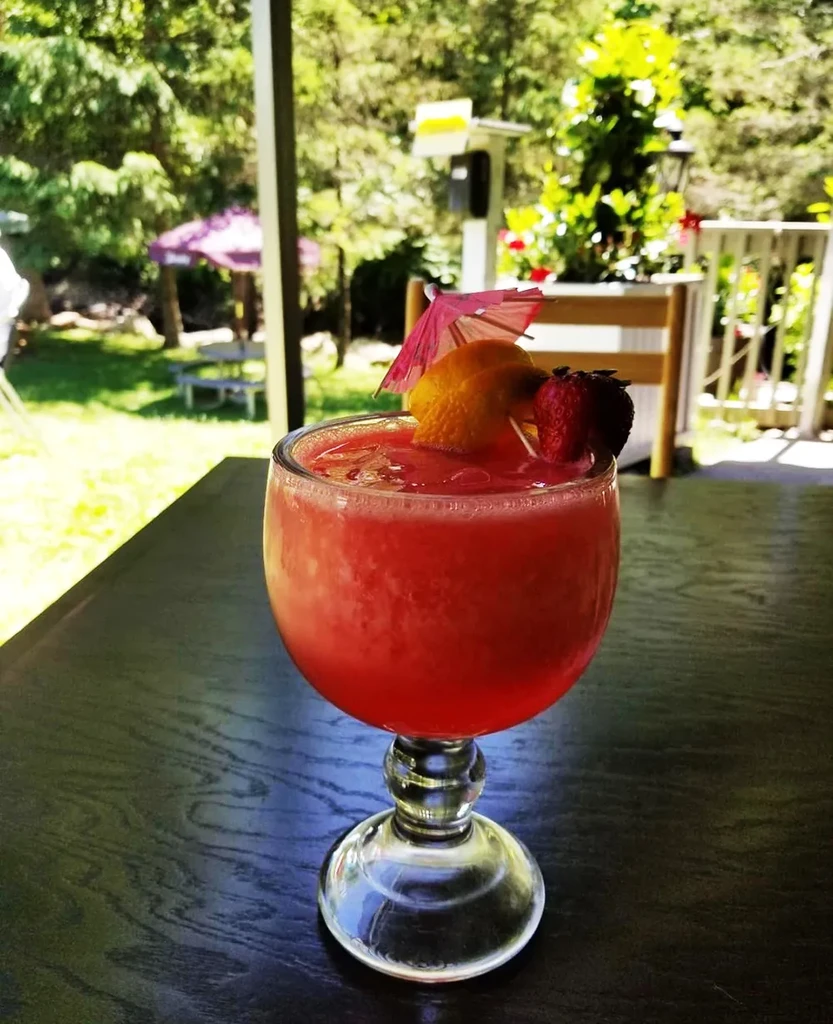 Red frozen cocktail with umbrella, citrus, and berries on patio.