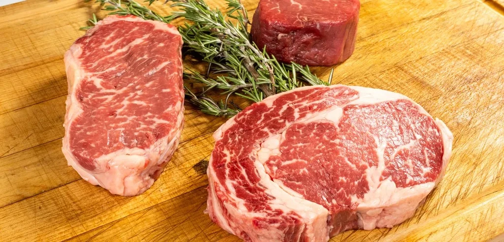 Raw New York, ribeye, and filet mignon steaks with rosemary on board.