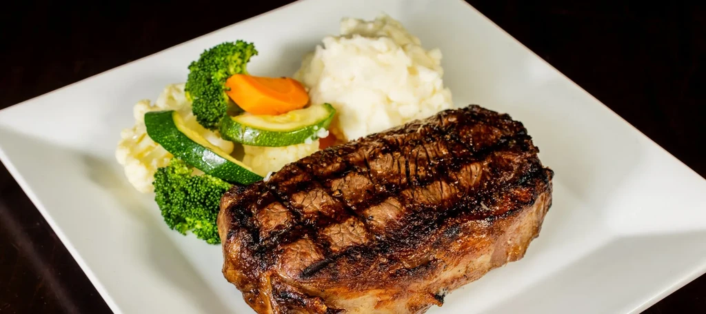 A well-plated grilled steak, mashed potatoes, and assorted vegetables.