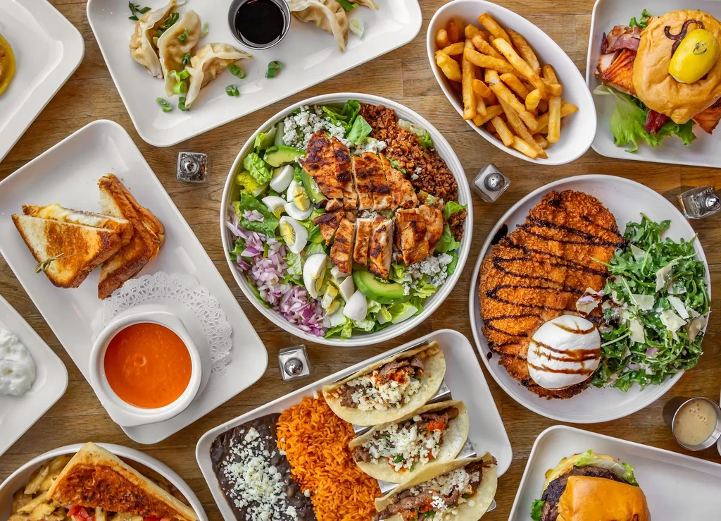 Overhead view of a diverse food spread on a light wooden table.