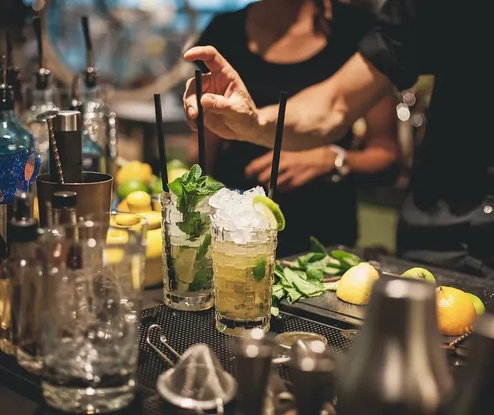 Hand adjusting two mint cocktails with lime at a dimly lit bar.