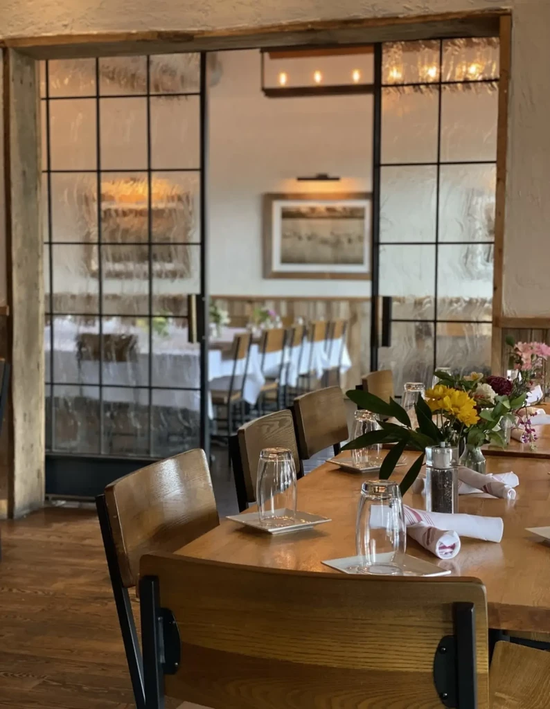 Modern rustic restaurant interior with long wooden table and floral centerpiece.