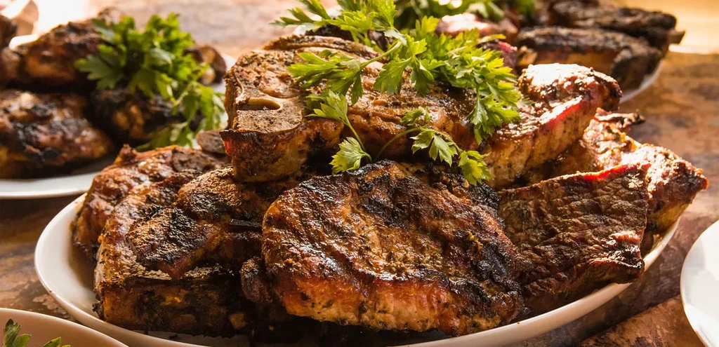 Piled grilled meat chops with grill marks and parsley garnish.