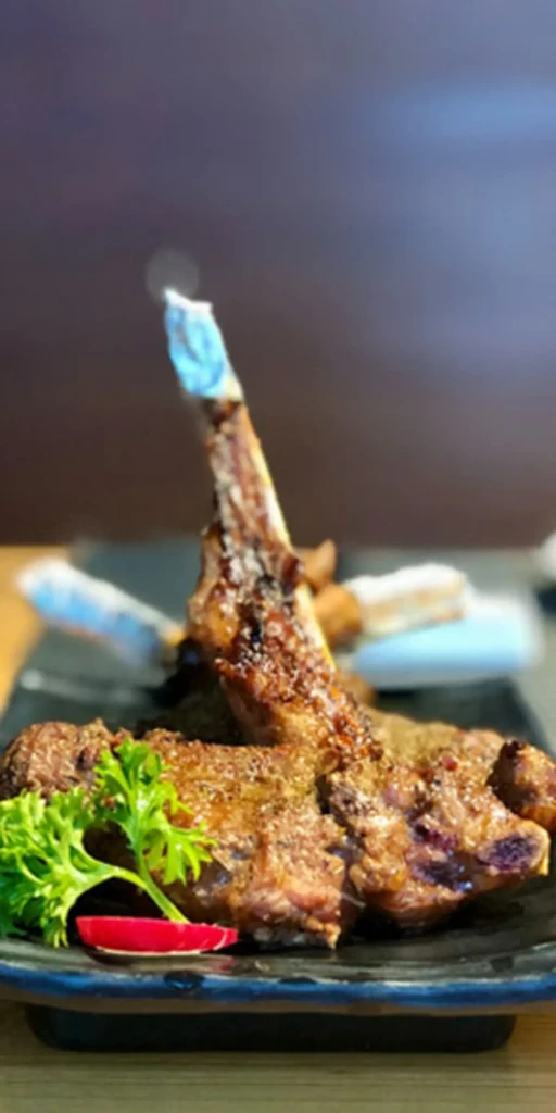 Seasoned grilled lamb chops on a plate with parsley and chili.