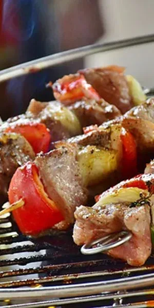 Multiple meat, bell pepper, and onion skewers cooking on a grill.