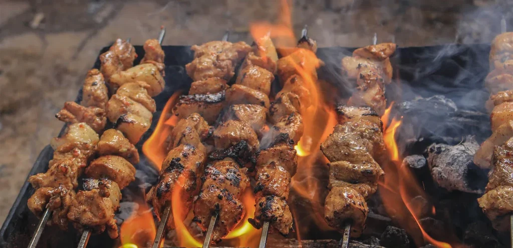 Skewers of seasoned meat grilling over open flames with smoke.