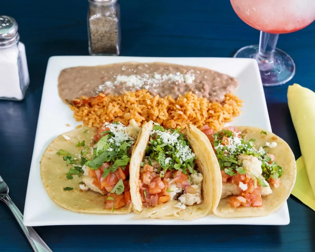 Overhead view of three tacos, rice, beans, and a pink drink.