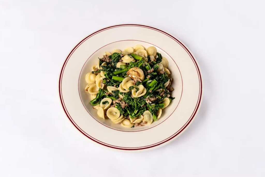 Orecchiette pasta with broccoli rabe and crumbled sausage on a white plate.