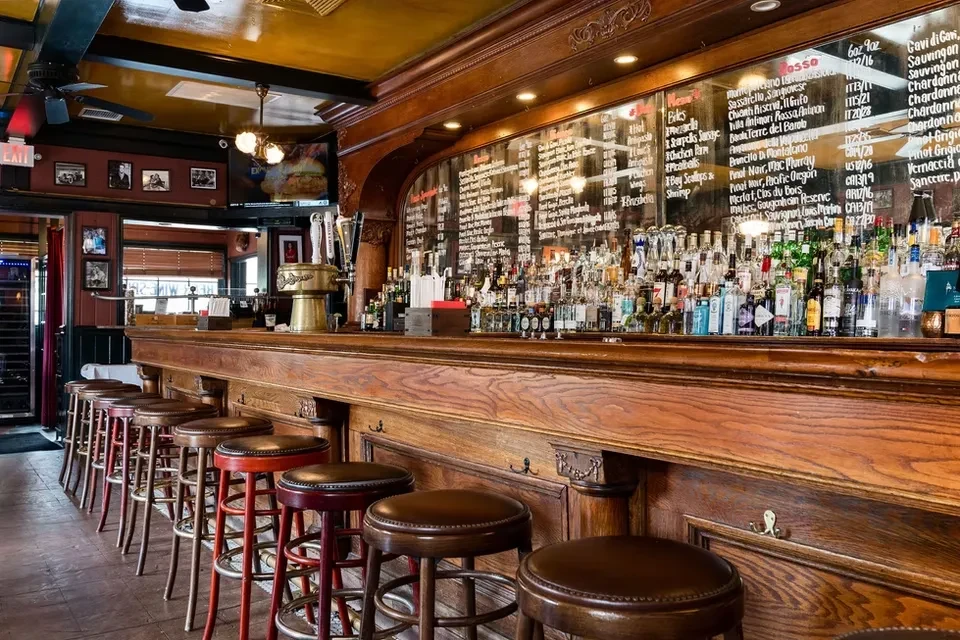 An empty wooden bar with multiple stools and bottles of alcohol.