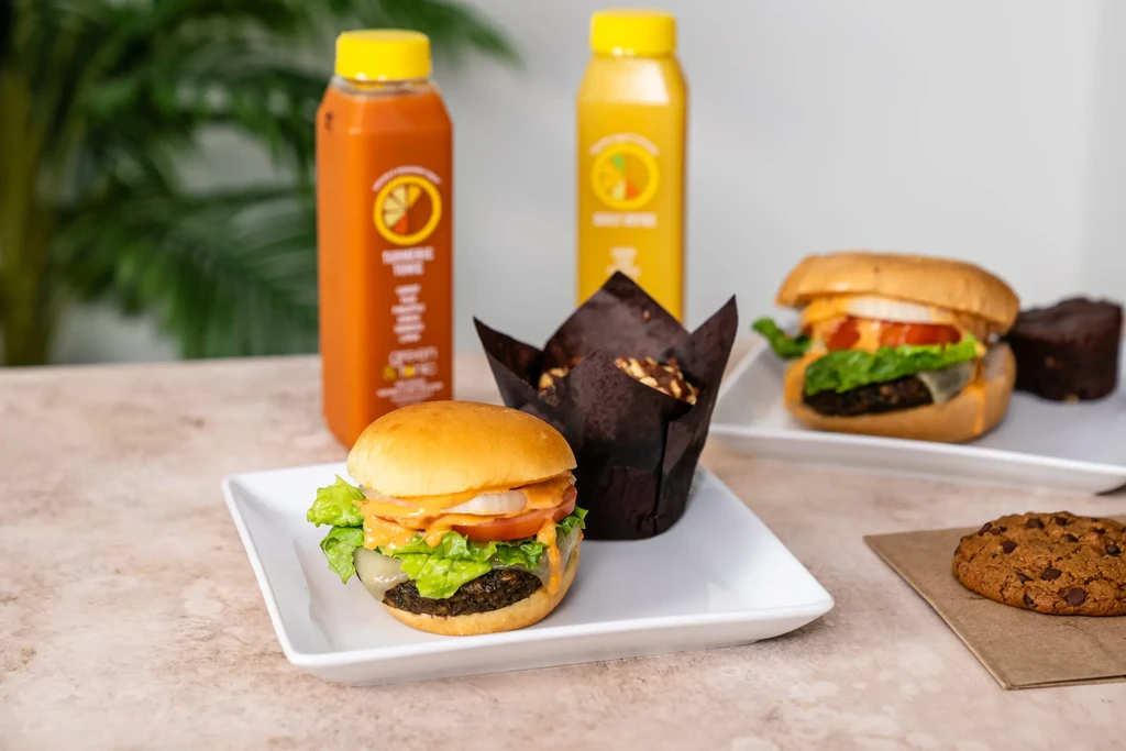 Two burgers, two juices, muffins, brownie, and cookie on a table.