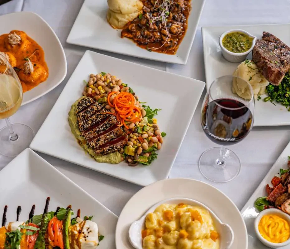 Various plates of food with wine on a white tablecloth.