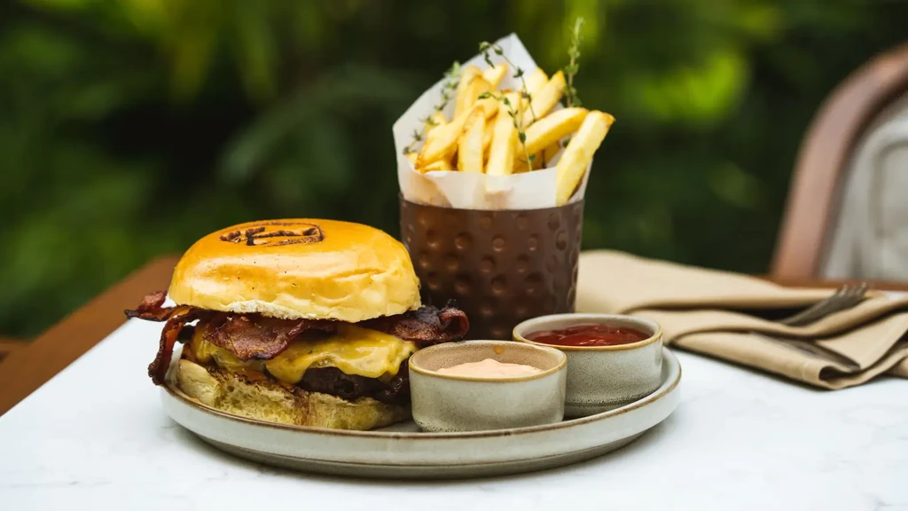 Bacon cheeseburger, french fries, and two dipping sauces on a table.